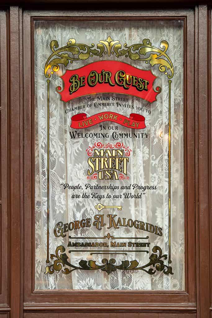 Etched glass door welcomes guests with "Be Our Guest" in classic Disney font, framed by ornate designs and a lace curtain behind—bringing the elegance and enchantment of a Disney celebration to your event.