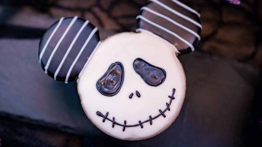 A festive Mickey-shaped cookie styled after Jack Skellington, featuring smooth white icing and bold black accents—an imaginative Disneyland dessert crafted especially for fans celebrating The Nightmare Before Christmas.