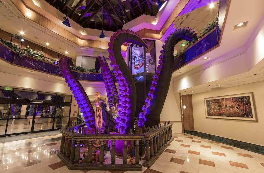 Immense purple tentacles emerge from a wooden set piece in a dazzling hotel lobby with marble floors, capturing the thrilling spectacle and fantastical design you’d expect from an immersive Disneyland attraction brought to life indoors.
