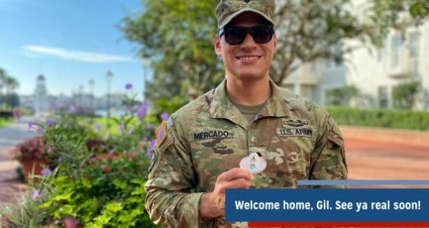 A U.S. Army soldier, all smiles in full uniform, stands outdoors at Disney Parks holding a celebratory Disney pin and a “Welcome home” message—capturing the heartfelt magic of a hero’s return to the Happiest Place on Earth.
