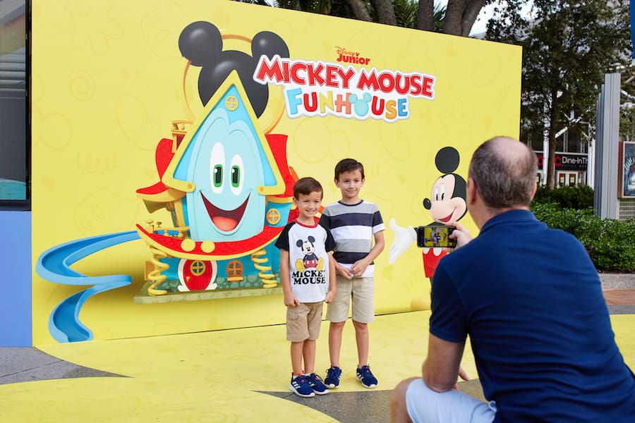 Two young Disney fans smile for a photo in front of the vibrant Mickey Mouse Funhouse backdrop at the Disney Junior Pop Up event, celebrating the magic of Mickey and friends.