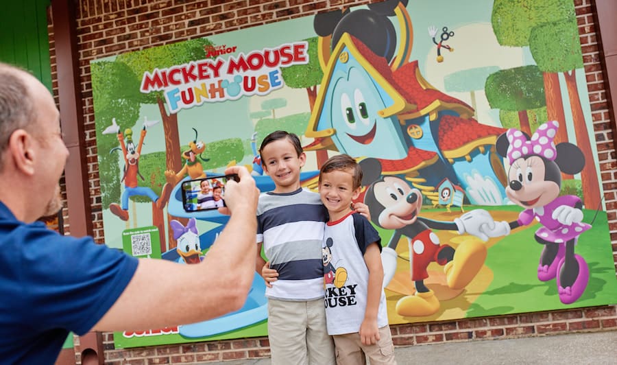 Two boys happily pose for a photo in front of the vibrant Mickey Mouse Funhouse mural at the Disney Junior Pop Up inside Disney Springs, capturing the joyful atmosphere of this family-friendly destination.