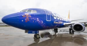 A Southwest Airlines jet featuring the "50 years" anniversary logo and an adorable bear graphic on its blue fuselage sits on a rain-soaked tarmac, celebrating the magic of Disney Parks with a playful nod to beloved characters and decades of family fun.
