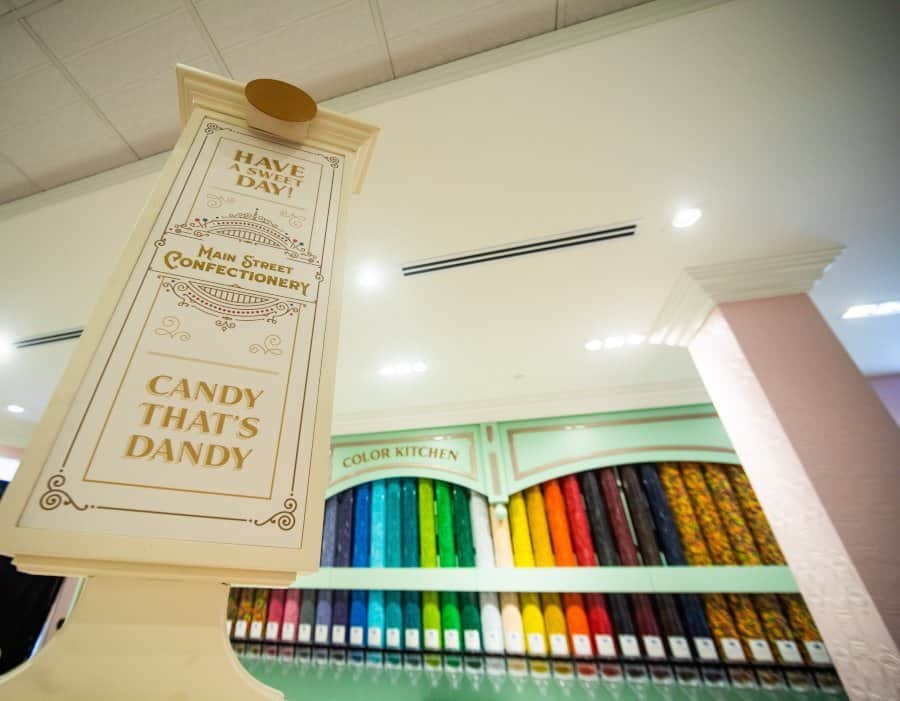 The iconic “Candy That’s Dandy” sign rises above the Main Street Confectionery at Magic Kingdom Park, with vibrant displays of sweets and treats behind it, celebrating the grand reopening for delighted park guests.