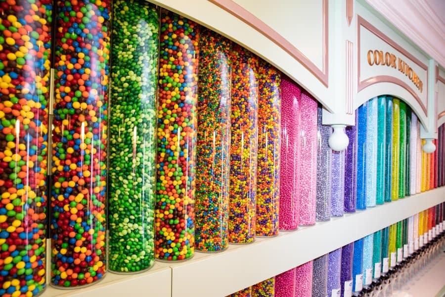 Rows of dazzling, clear tubes brimming with vibrant candy beads create a rainbow spectacle on the display wall, setting a whimsical scene for guests returning to the freshly reopened Main Street Confectionery in Magic Kingdom.