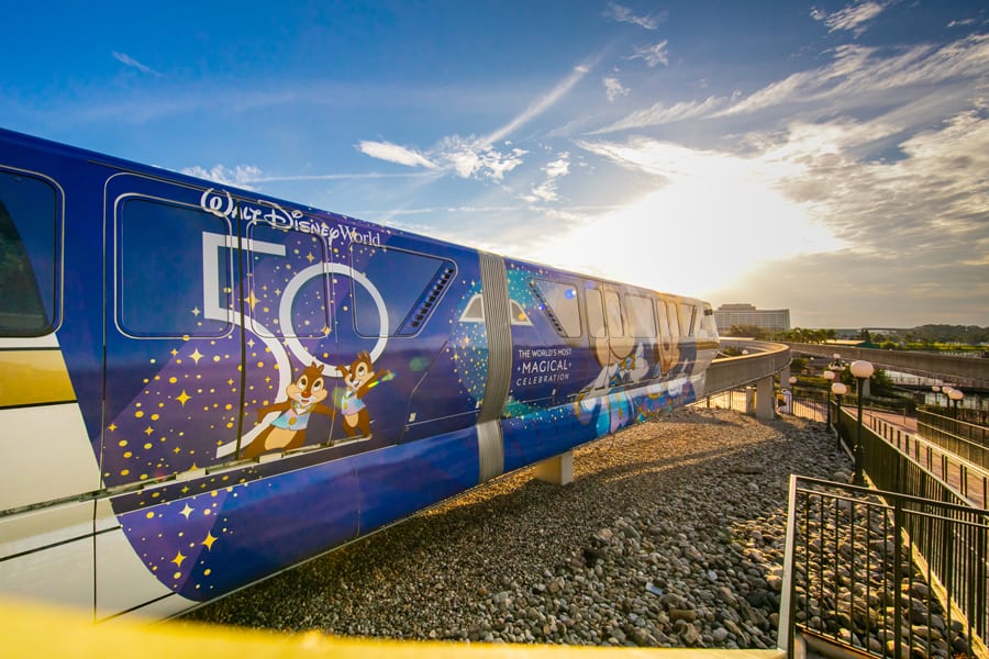 The Disney World monorail, sparkling with celebratory Extra Pixie Dust for the 50th Anniversary, glides along its track against a magical sunset backdrop.