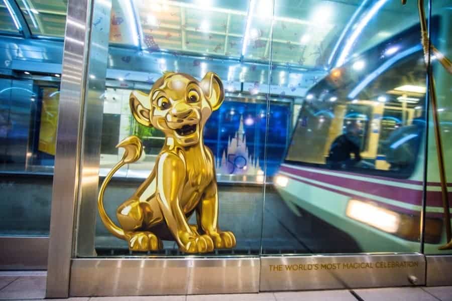A shimmering gold Simba decal adorns the glass at a Walt Disney World Resort train station, embodying Disney Style as the iconic monorail glides by in the background and bringing the enchantment of Disney travel to life.