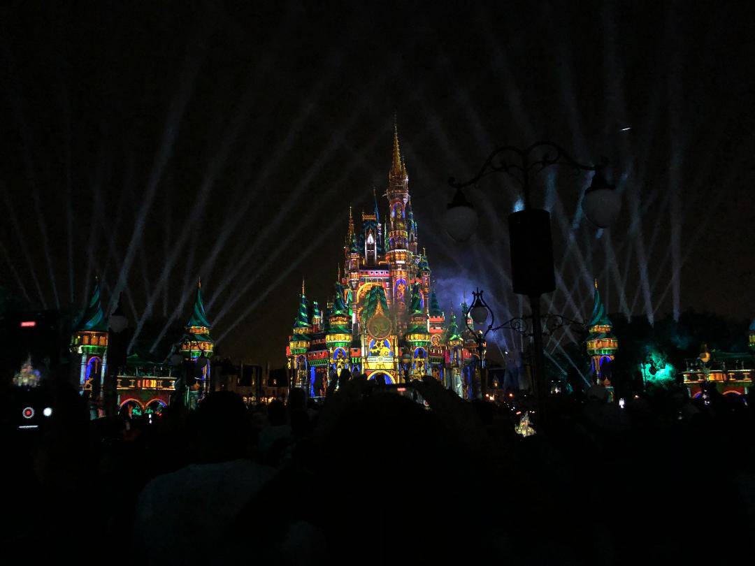Cinderella Castle shines brilliantly at night, aglow with colorful lights and lasers, enchanting Magic Kingdom guests gathered below as dazzling fireworks explode above during the iconic Happily Ever After nighttime spectacular.