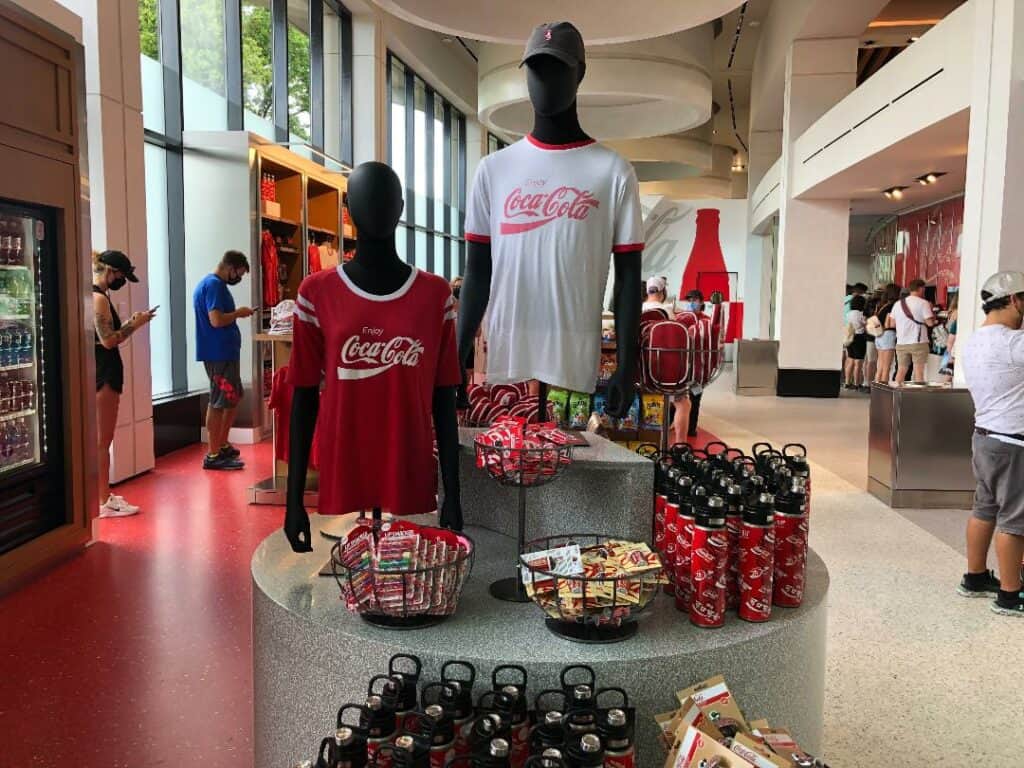 Club Cool’s vibrant Coca-Cola display showcases branded shirts, collectible bottles, and snacks under bright lights, with excited guests snapping photos to celebrate its grand return at EPCOT.