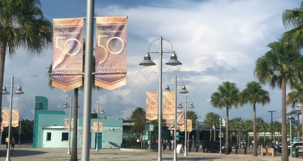 The entrance plaza at Disney’s Hollywood Studios lined with iconic palm trees and festive 50th Anniversary Banners, set against a backdrop of blue skies and fluffy clouds.