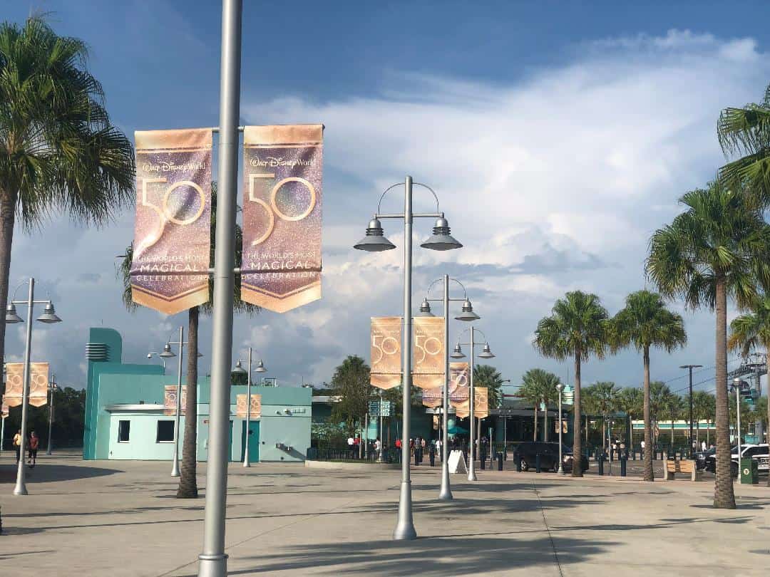 The entrance plaza at Disney’s Hollywood Studios lined with iconic palm trees and festive 50th Anniversary Banners, set against a backdrop of blue skies and fluffy clouds.