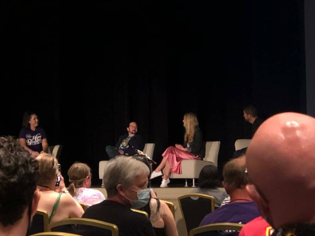 Linda Larkin and John Morris join two others onstage for a lively Disney panel discussion, as fans in the audience—including some wearing face masks—capture the moment with excitement.