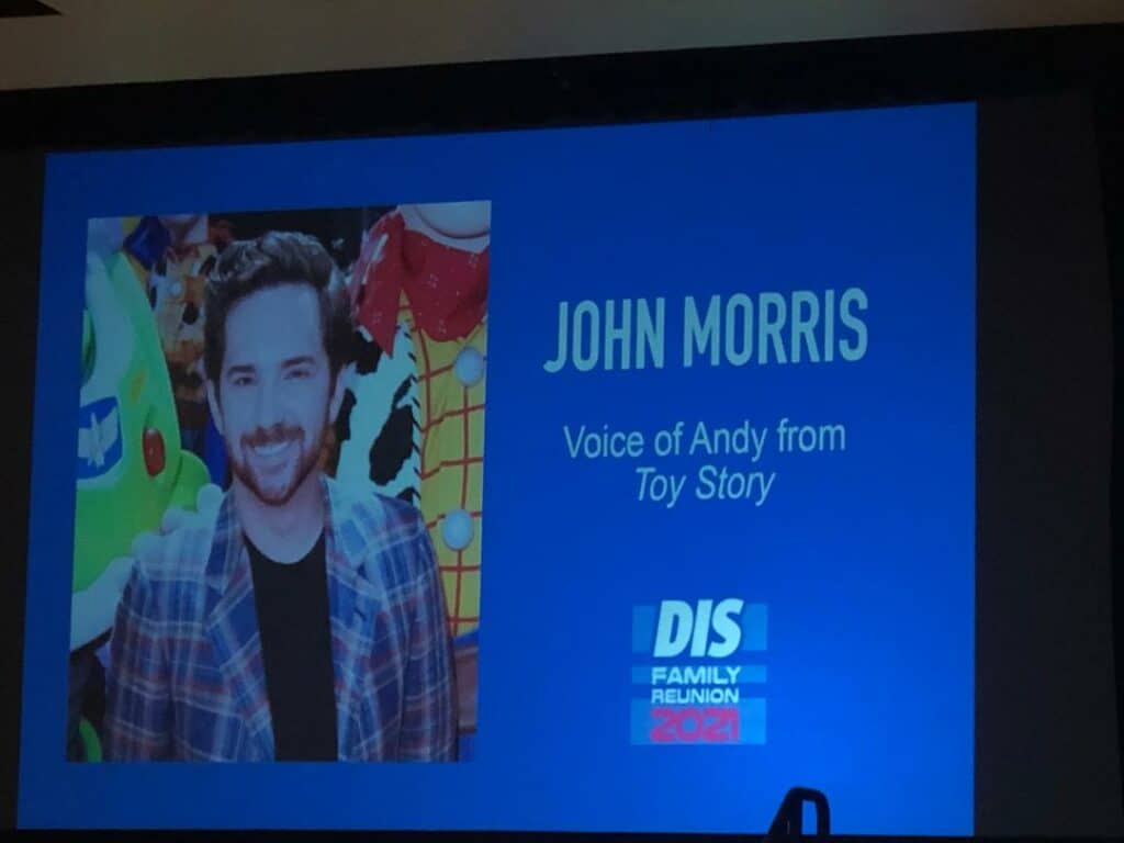 John Morris, known as the voice of Andy from Toy Story, stands in front of a blue backdrop displaying "DIS Family Reunion 2021" during his panel at the event, joined by special guest Linda Larkin.