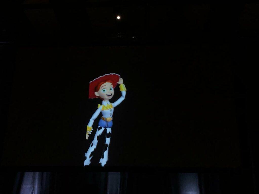 Jessie from Toy Story waves enthusiastically under a spotlight, just like you’d see her greeting fans at a Disney park attraction or making an appearance during a special panel event.