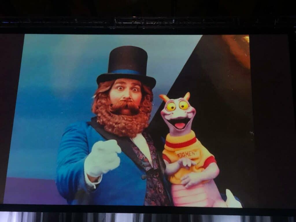 Dreamfinder, in his signature blue coat and top hat, poses with Figment—the beloved purple dragon sporting a yellow shirt—set before the energetic scene of iconic EPCOT attractions, capturing the spirit of classic Actor Panel moments cherished by Disney fans.