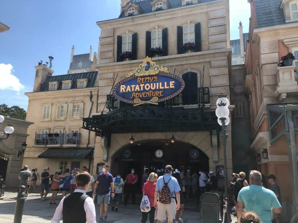 Fans line up outside Remy's Ratatouille Adventure, set against charming Parisian architecture at EPCOT, excited for their turn to enjoy this immersive Disney World experience on a bright, sunny day.