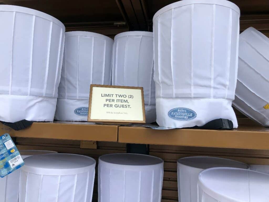 Chef hats line a display shelf with a sign that says "Limit two (2) per item, per guest," ready for Passholder previews at the park.