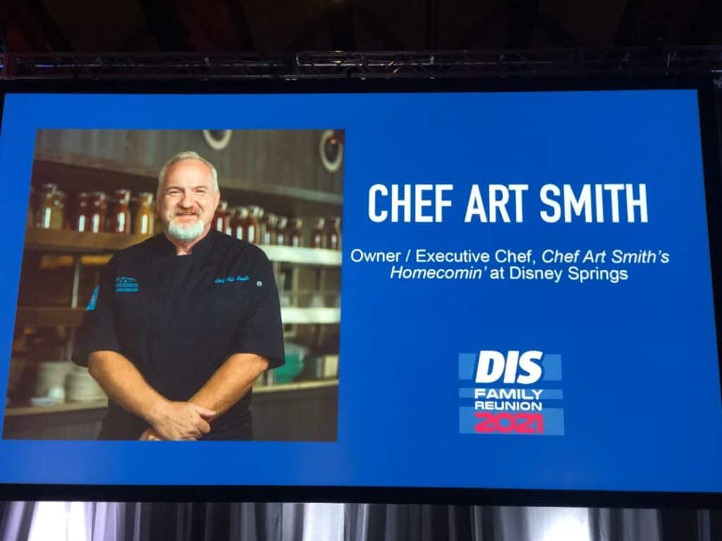 Chef Art Smith beams onstage beside the vibrant DIS Family Reunion 2021 sign, excited to entertain and inspire fans as a special panel guest at this ultimate Disney fan event.