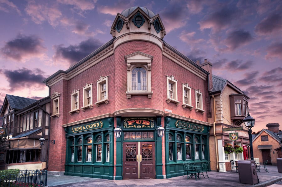 The Rose & Crown, a classic red-brick British pub with green trim and large inviting windows, glows at sunset in the heart of the park’s lively entertainment district—a welcoming spot to unwind after a day of attractions and shows.