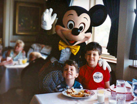 Mickey Mouse shares a magical moment with two delighted kids at a Disney World restaurant table, one proudly sporting a name tag—celebrating 50 incredible years of Walt Disney World memories.