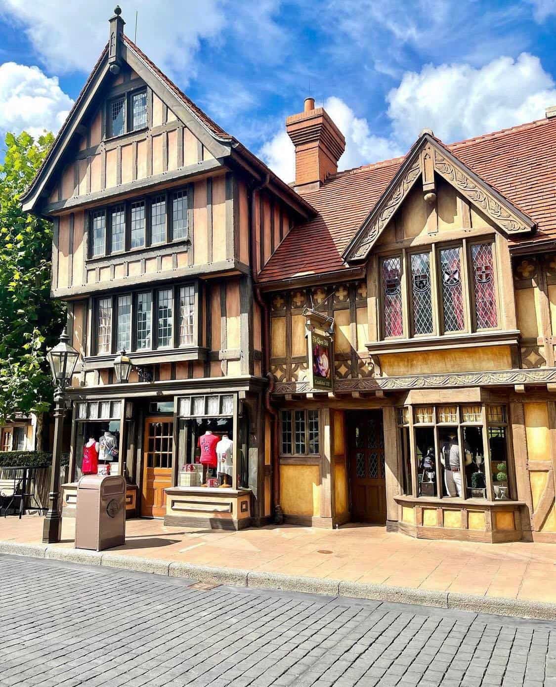Charming Old English storefront with signature timber framing and a classic red roof, displaying mannequins in the window under bright sunshine—classic EPCOT United Kingdom Pavilion architecture that transports guests to an authentic British village within Walt Disney World.
