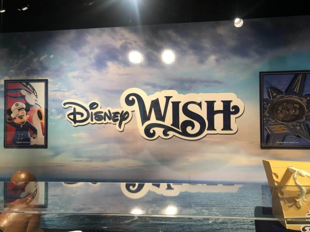 The Disney Wish logo shines against a vibrant ocean-themed wall, flanked by framed Mickey Mouse artwork and a medallion, evoking the nostalgic elegance of Disney's Hollywood Studios atmosphere.