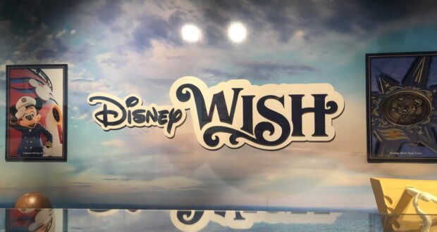 The Disney Wish logo shines against a vibrant ocean-themed wall, flanked by framed Mickey Mouse artwork and a medallion, evoking the nostalgic elegance of Disney's Hollywood Studios atmosphere.