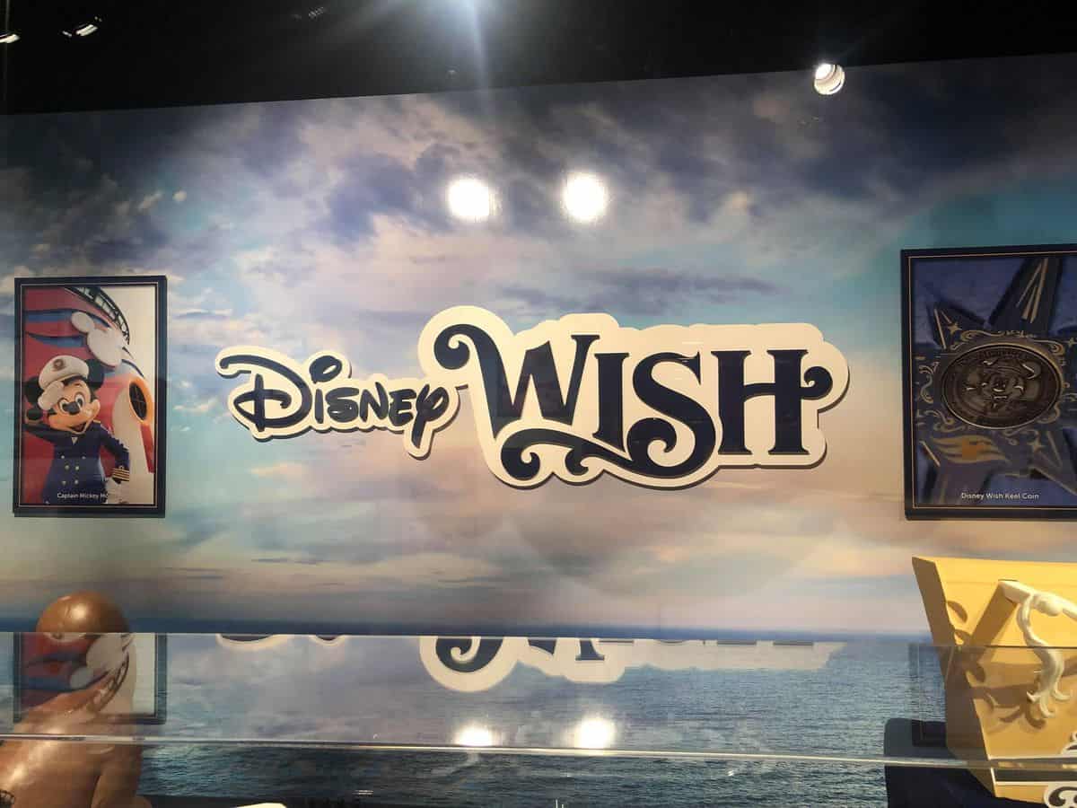 The Disney Wish logo shines against a vibrant ocean-themed wall, flanked by framed Mickey Mouse artwork and a medallion, evoking the nostalgic elegance of Disney's Hollywood Studios atmosphere.