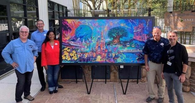 Five Disney fans gather around a vibrant painting celebrating Walt Disney World's 50th Anniversary, showcased on an easel outdoors in the park.