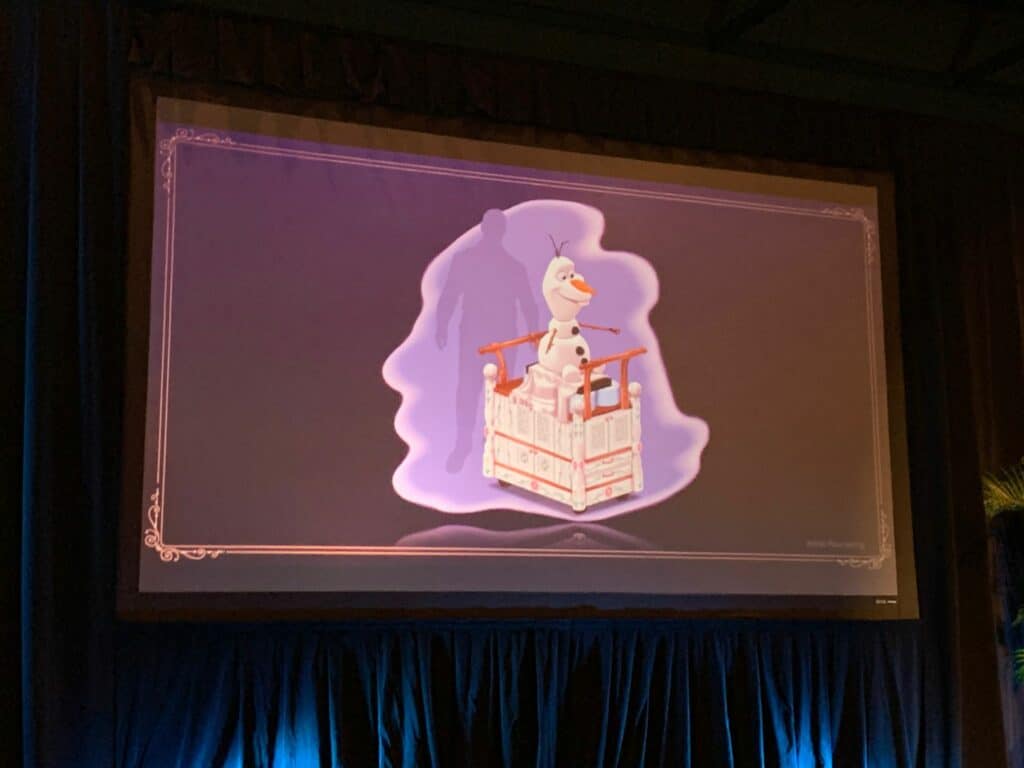 Olaf from Frozen appears on screen inside a crate, highlighted by a purple silhouette backdrop, capturing the playful magic of the Frozen Dining Adventure aboard the Disney Wish.