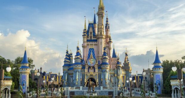Cinderella Castle at Disney World stands tall with its iconic blue and gold spires beneath a partly cloudy sky, inviting guests to embrace the enchantment and enter for a chance to win exclusive Disney merchandise during their visit.