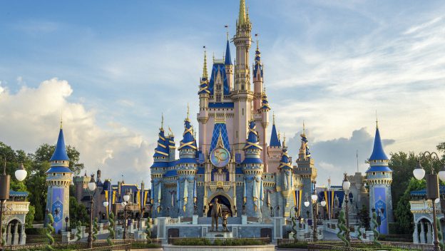 Cinderella Castle at Disney World stands tall with its iconic blue and gold spires beneath a partly cloudy sky, inviting guests to embrace the enchantment and enter for a chance to win exclusive Disney merchandise during their visit.