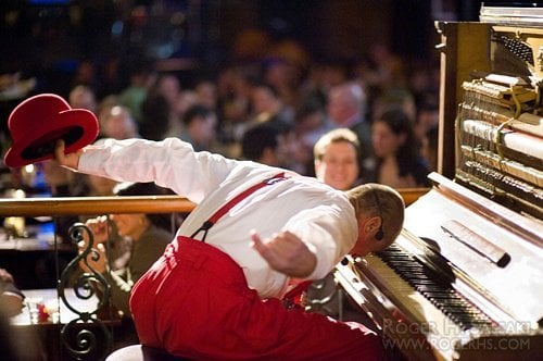 Yehaa Bob, wearing his signature red suspenders, takes a bow at his piano while holding a red hat, as fans in the audience cheer him on during his high-energy show at Disney’s Port Orleans Resort.