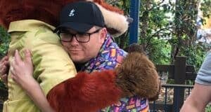 A guest wearing glasses shares a warm hug with Baloo from The Jungle Book, surrounded by lush greenery and a rustic wooden fence, evoking the spontaneous magic of Disney’s Imagineering in Florida where beloved characters create unforgettable moments beyond the parks’ main attractions.