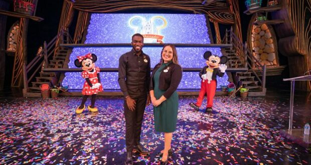 Guests celebrate on a confetti-strewn stage at Disneyland, posing with Minnie Mouse and Mickey Mouse while the Disneyland Team joins in the festivities.