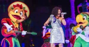 A dazzling singer in a sparkling silver dress takes center stage, joined by beloved Disney characters in vibrant costumes playing instruments, setting the scene for an enchanting holiday performance at Walt Disney World.