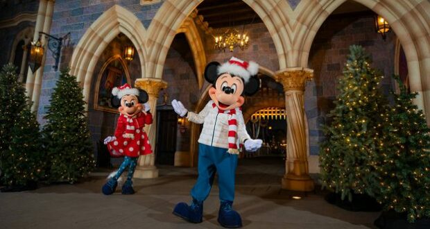 Mickey and Minnie don charming winter attire as they pose together beside brilliantly decorated trees in front of the iconic Disneyland castle, capturing the festive spirit of the park during its beloved Holiday Collection celebration.