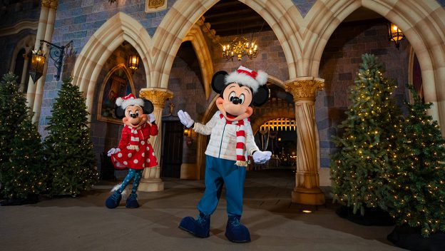 Mickey and Minnie don charming winter attire as they pose together beside brilliantly decorated trees in front of the iconic Disneyland castle, capturing the festive spirit of the park during its beloved Holiday Collection celebration.