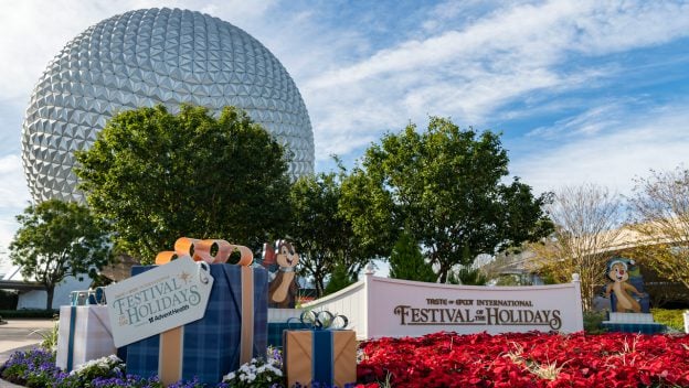 Spaceship Earth towers above cheerful Festival of the Holidays signage, colorful presents, and playful Chip and Dale decorations surrounded by vibrant flowers—an ideal photo spot for Annual Passholders to enjoy exclusive festival discounts and create lasting memories at EPCOT.