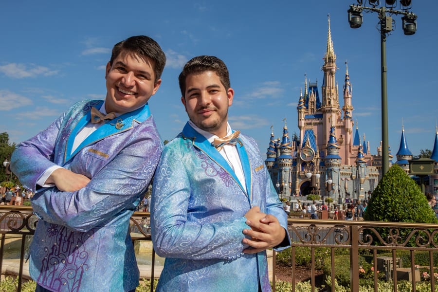 Two performers in dazzling blue suits smile for the camera in front of Cinderella Castle at Walt Disney World, joining the 50th Anniversary celebration under a bright Florida sky.