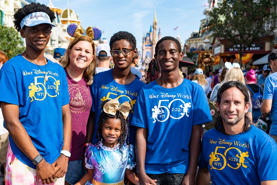 Six friends gather in front of Cinderella Castle at Disney World, joyfully celebrating the park’s 50th anniversary with festive energy.
