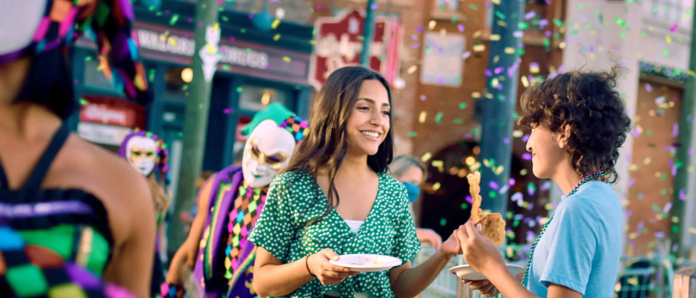 Revelers enjoy delicious bites and share smiles at Universal Orlando’s 2022 Mardi Gras celebration, surrounded by colorful confetti and energetic masked performers, capturing the excitement of this iconic theme park event.