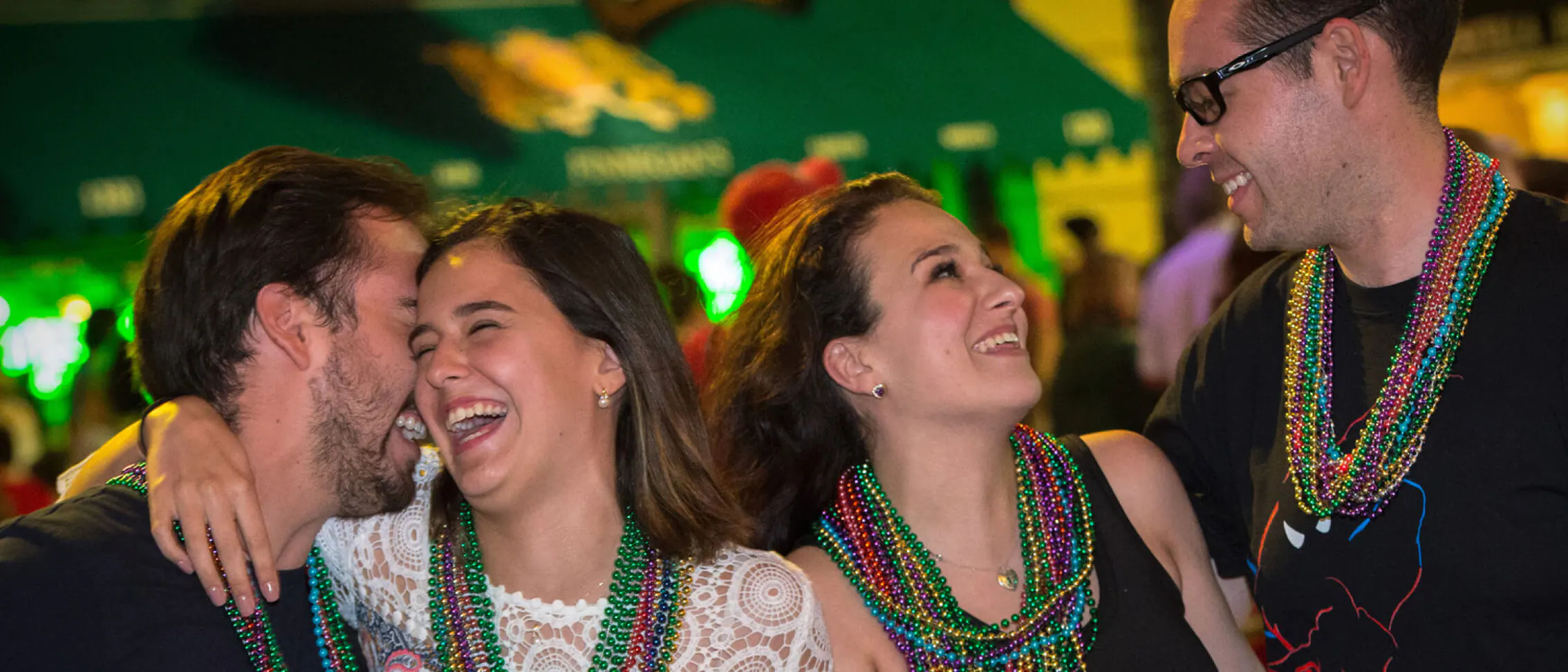 Groups of friends show off vibrant bead necklaces as they celebrate and enjoy the energy of Mardi Gras at Universal Orlando in 2022, laughing and smiling amid the festive atmosphere.