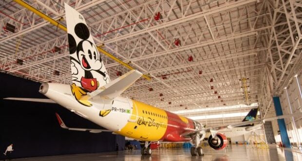 A vibrant Disney-themed plane featuring Mickey Mouse on its tail waits inside a spacious hangar, ready to whisk guests away for magical adventures above Brazil.