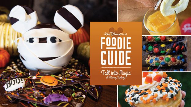 Halloween-themed Mickey mummy treat and festive desserts on display alongside a vibrant orange "Foodie Guide" sign, inviting guests to indulge in Magic Treats at Disney Springs.