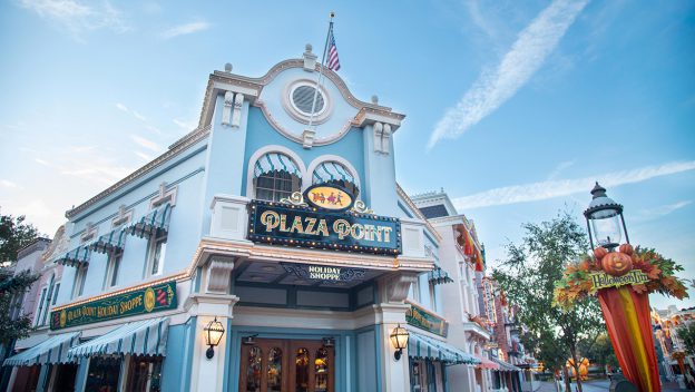 Plaza Point at Disneyland, a cheerful light blue storefront topped with an American flag and adorned in festive fall decorations, welcomes guests to explore its all-new holiday-themed shopping experience right on Main Street, U.S.A.