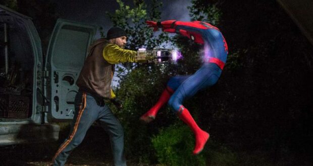 Electro unleashes a powerful surge from his weapon, sending Spider-Man soaring backward in an electrifying nighttime battle scene near a parked van.
