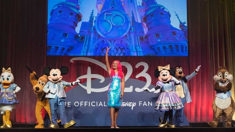 Mickey Mouse, Minnie Mouse, Donald Duck, Goofy, Pluto, and Daisy Duck join a Disney host onstage at Destination D23, with a magical castle backdrop—capturing the spirit of a Sunday Recap for Disney fans.