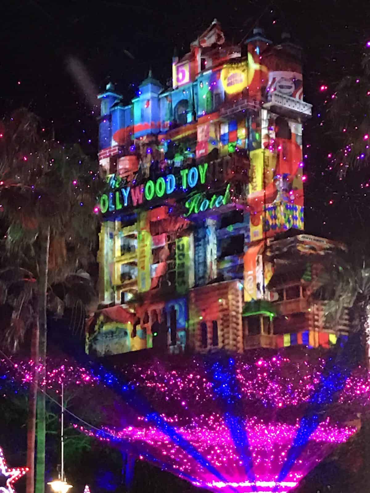 The iconic Hollywood Tower Hotel glows with vibrant lights and dazzling projections emblazoned with "HOLLYWOOD TOY Hotel," as the Return of Sunset celebration brings Disney's holiday magic to life after dark.