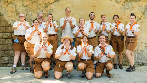 Wilderness Explorer scouts at Disney’s Animal Kingdom group together in their signature brown uniforms, all smiling and flashing the iconic "W" hand sign for a fun team photo.